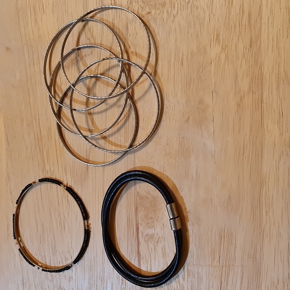 Set of 7 bracelets. 5 are silver tone hammered metal, 1 leather like, 1 black